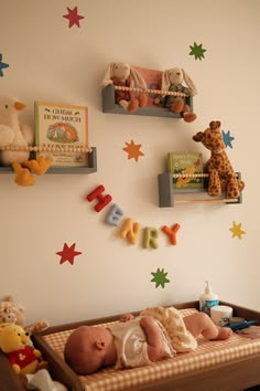 Nursery wall with colorful felt stars, wooden picture-book ledges, stuffed animals, and cut-out letters spelling a baby's name