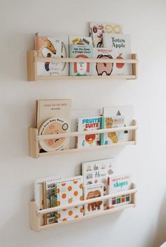 Three wooden wall ledges displaying picture books face-out against a plain white wall