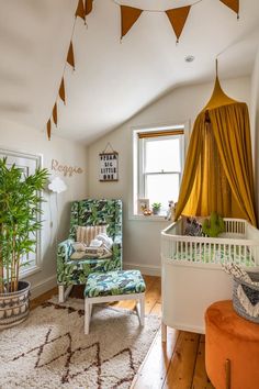 Attic nursery nook with a mustard canopy, felt pennant bunting, a leafy patterned armchair, plants, and a woven rug